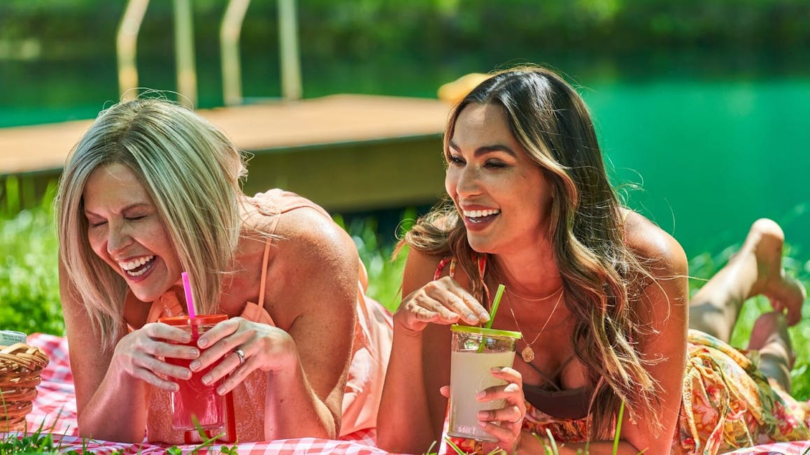 Women Laughing And Enjoying Drinks On Picnic Blanket