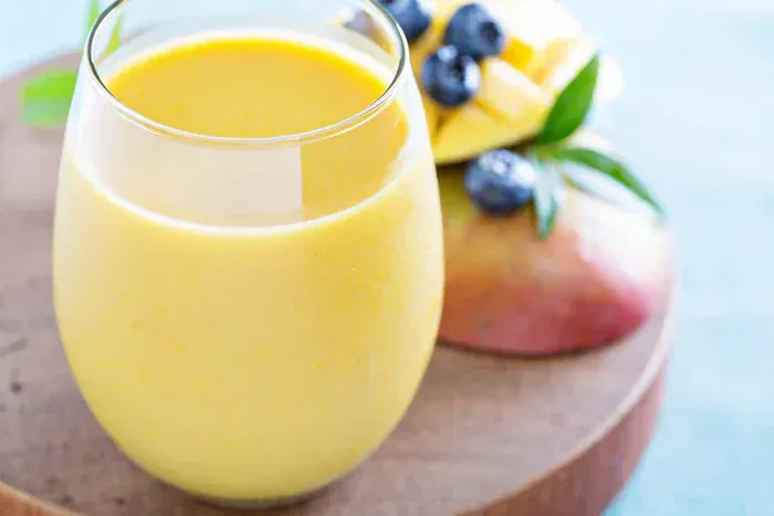 An orange smoothie in a glass with fruit behind it.