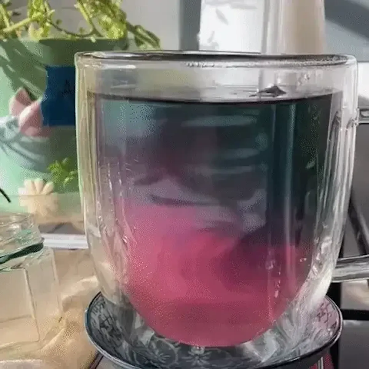 A glass straw is stirring a glass of butterfly pea flower tea. It turns from blue to pink.