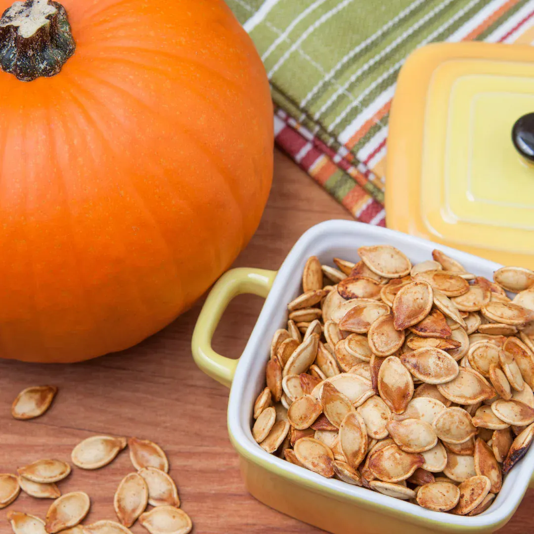 A pumpkin on a table next to a bowl of pumpkin seeds.