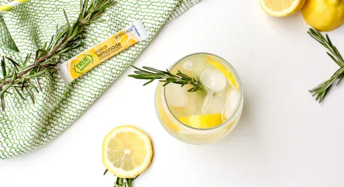A glass of rosemary lemonade alongside a True Lemon Original Lemonade packet.