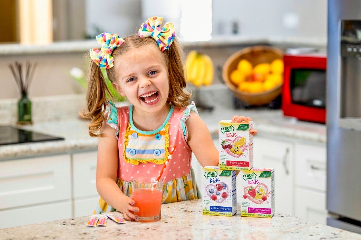 Two children in a white kitchen stirring True Lemon packets into their glasses of water