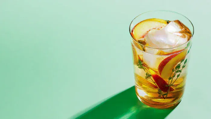A glass of peach green tea punch on a green background.