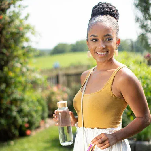 A woman is in a garden holding a water bottle.