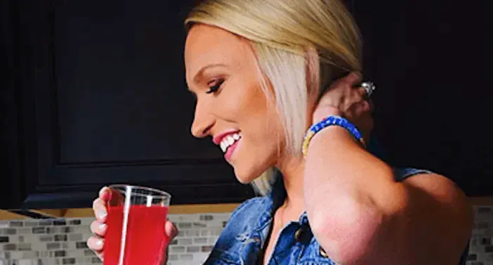 Alysha looks to the side, smiling as she holds a glass of True Lime Black Cherry Limeade.