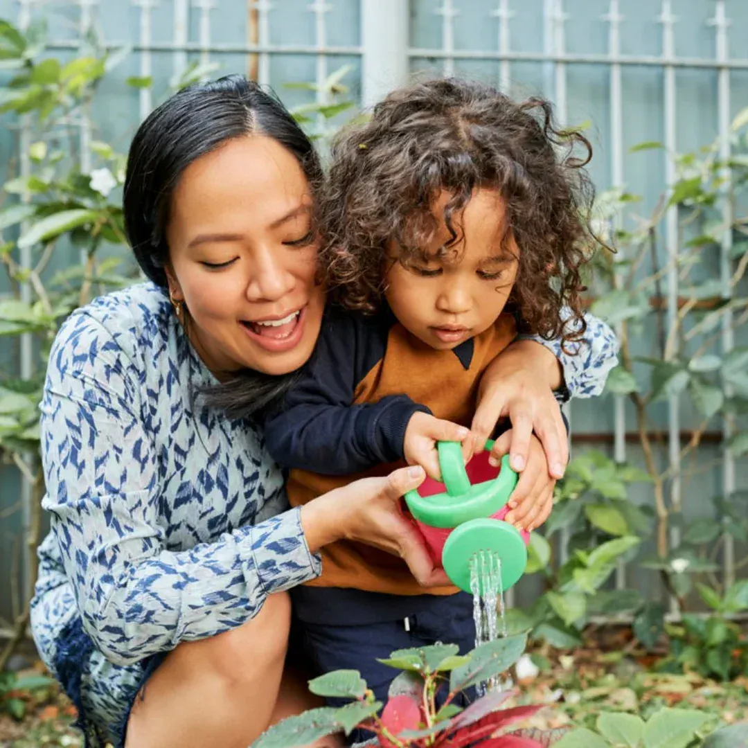 A woman and her child watering a plant in the garden.