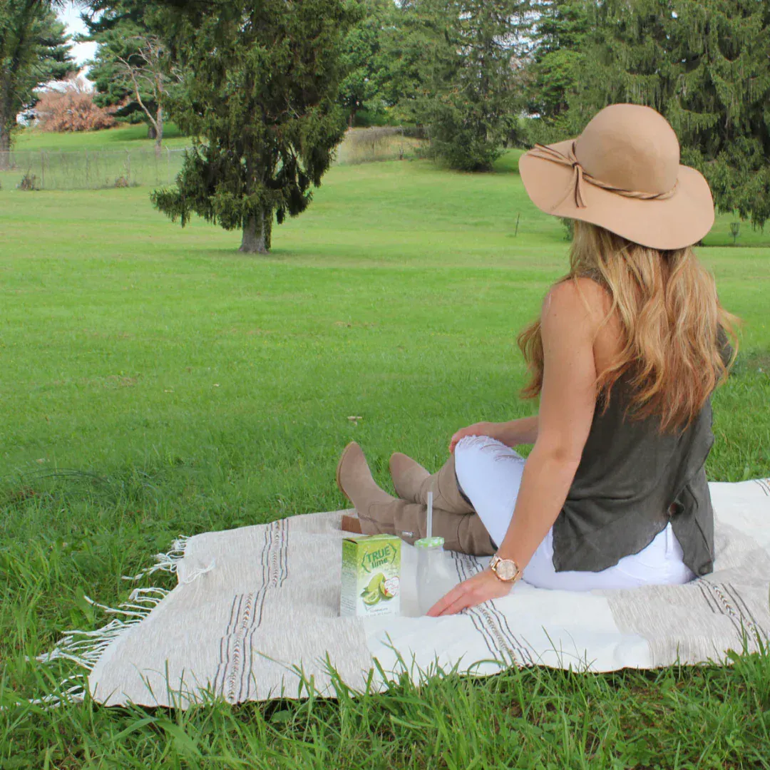 A woman sitting on a picnic blanket on a hill. Next to her is a box of True Lime.