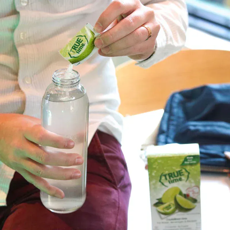 A person is sitting down pouring True Lime in a water bottle.