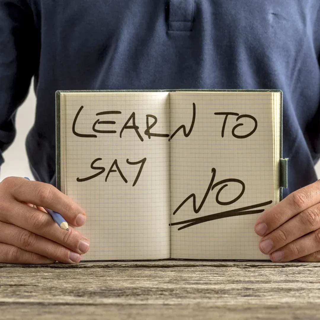 A man holding up a notebook that says "Learn to say no."