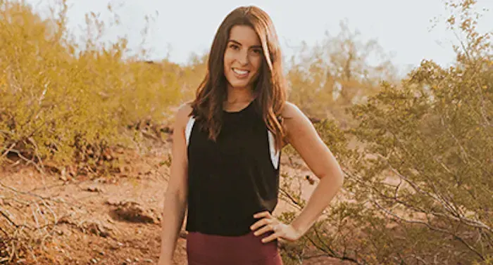 Brooke is standing on a sandy hill. She has one hand on her hip and she is smiling.