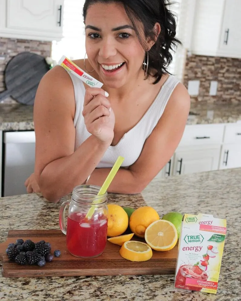 A woman holding up an True Energy packet in her kitchen.