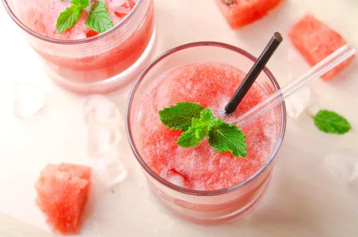 A cherry-melon mojito cooler in a glass next to some ice and watermelon.