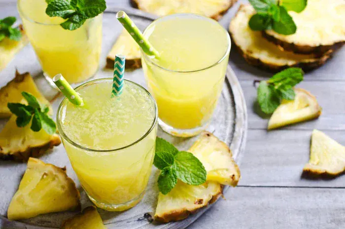 A tray of 3 glasses of True Lime Pineapple Mint Punch. There are slices of pineapple around it.