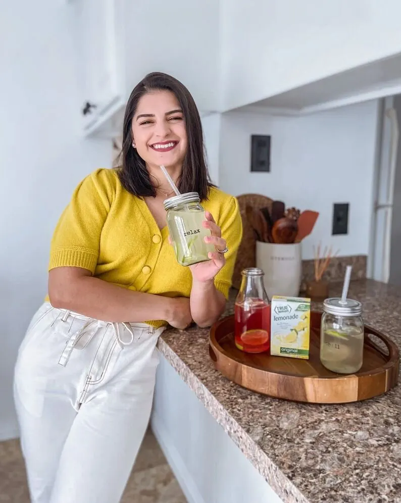 A woman is holding a glass of lemonade and leaning on a counter.