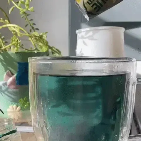 A packet of True Lemon is being poured into a cup of butterfly pea flower tea. The blue tea turns pink.