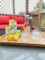 A man is sitting on a couch holding a glass of water. There is a box of True Lemon next to him.