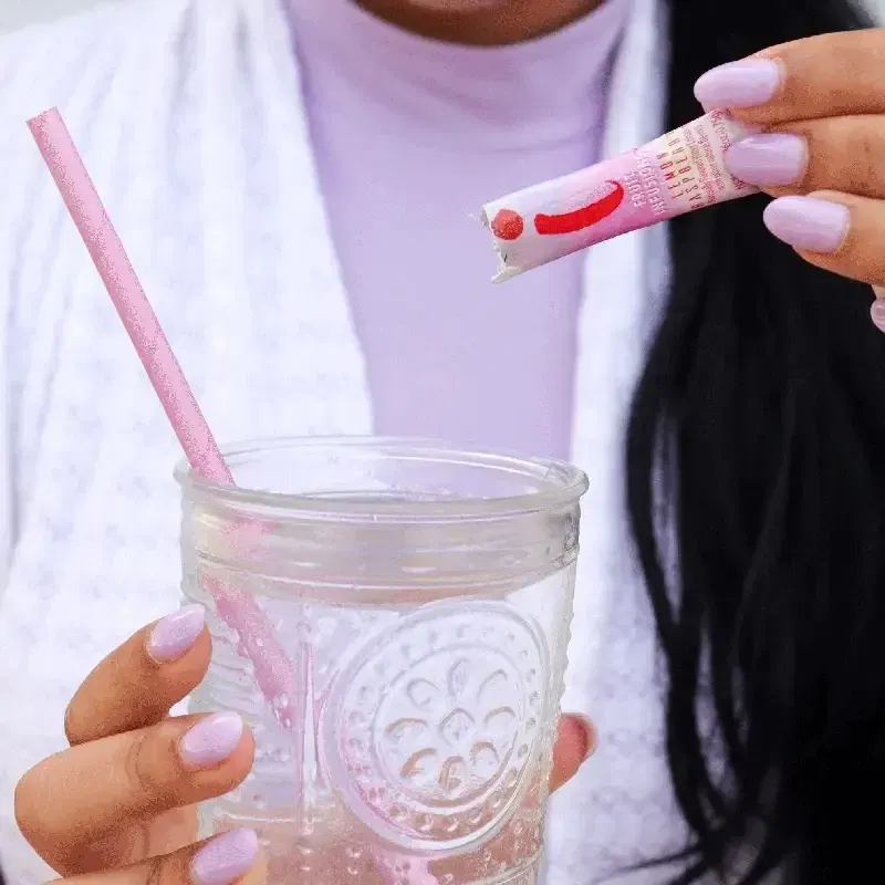 A woman is pouring a packet of True Citrus Fruit Infusions into a glass of water.